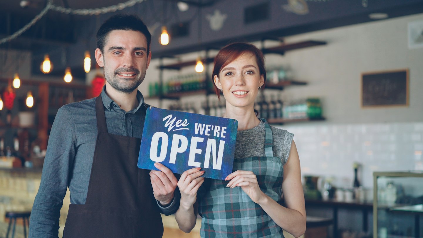 Dos dueños de negocios sosteniendo un cartel de "abierto" en su tienda.